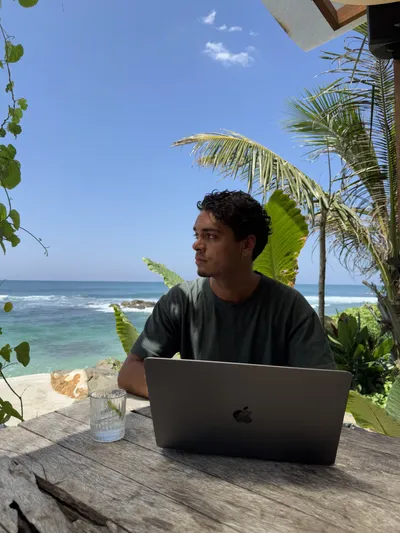 Djenthan working on a laptop at the beach