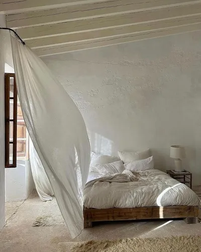 Linen curtain blowing over a bed